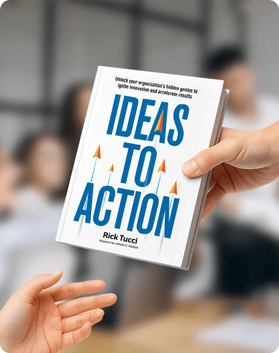 Ideas to Action book cover by Rick Tucci, held in a workplace setting