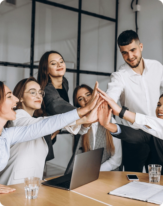 Diverse business team giving a group high-five around a table during an Ideas-to-Action team meeing.